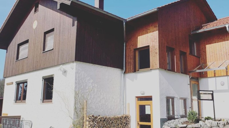 Zweistöckiges Gebäude mit Holzverkleidung und weißem Putz, gepflasterter Hof, Brennholzstapel, blauer Himmel. Zweistöckiges Gebäude mit Holzverkleidung und weißem Putz, gepflasterter Hof, Brennholzstapel, blauer Himmel.