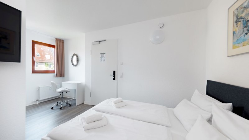 Helles Doppelzimmer mit zwei Betten, einem Schreibtisch und Stuhl. Ein Fenster mit Vorhang und ein Wandspiegel sind sichtbar., © Hotel Olgaeck Helles Doppelzimmer mit zwei Betten, einem Schreibtisch und Stuhl. Ein Fenster mit Vorhang und ein Wandspiegel sind sichtbar., © Hotel Olgaeck
