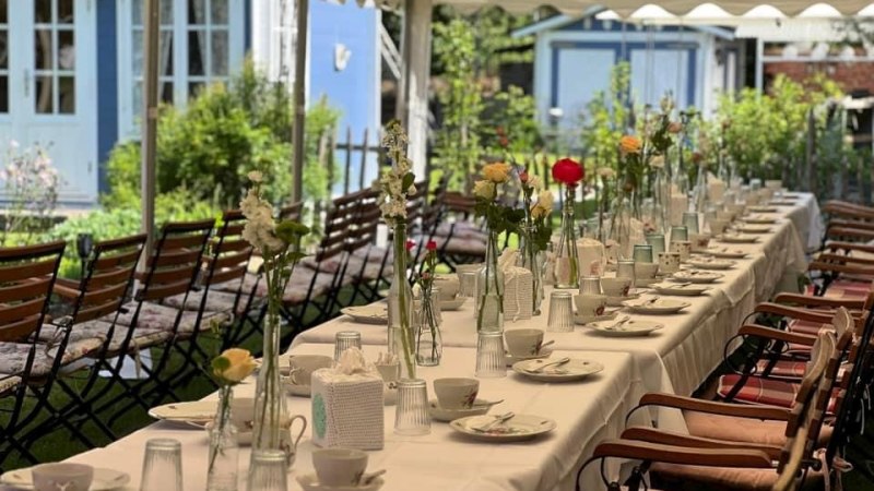 Ein langer Tisch unter einem Pavillon, festlich gedeckt mit Blumenvasen und Geschirr, vor einem blauen Geb&auml;ude im Garten., &copy; Caf&eacute;Pl&auml;tschwiesle