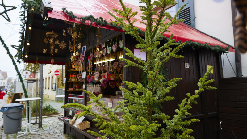 Ein Weihnachtsmarktstand mit roten Dach und Dekorationen. Lebkuchenherzen hängen aus. Ein Tannenzweig im Vordergrund., © SMG, Sarah Schmid Ein Weihnachtsmarktstand mit roten Dach und Dekorationen. Lebkuchenherzen hängen aus. Ein Tannenzweig im Vordergrund., © SMG, Sarah Schmid
