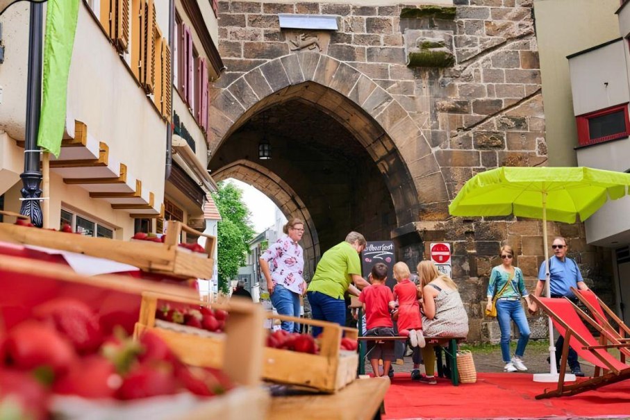 Menschen genießen ein Erdbeerfest vor einem alten Torbogen. Im Vordergrund sind Erdbeeren in Kisten, im Hintergrund ein grüner Sonnenschirm., © ©marketing-esslingen.de Menschen genießen ein Erdbeerfest vor einem alten Torbogen. Im Vordergrund sind Erdbeeren in Kisten, im Hintergrund ein grüner Sonnenschirm., © ©marketing-esslingen.de