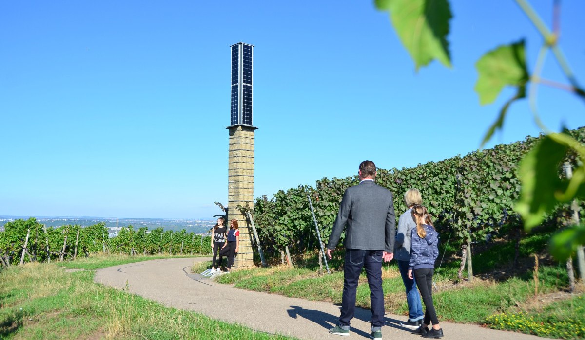 Menschen spazieren auf einem Weg durch die Weinberge in Fellbach. Ein hoher, schmaler Turm steht am Wegesrand. Der Himmel ist klar und blau., © Foto: Simone Mathias Menschen spazieren auf einem Weg durch die Weinberge in Fellbach. Ein hoher, schmaler Turm steht am Wegesrand. Der Himmel ist klar und blau., © Foto: Simone Mathias