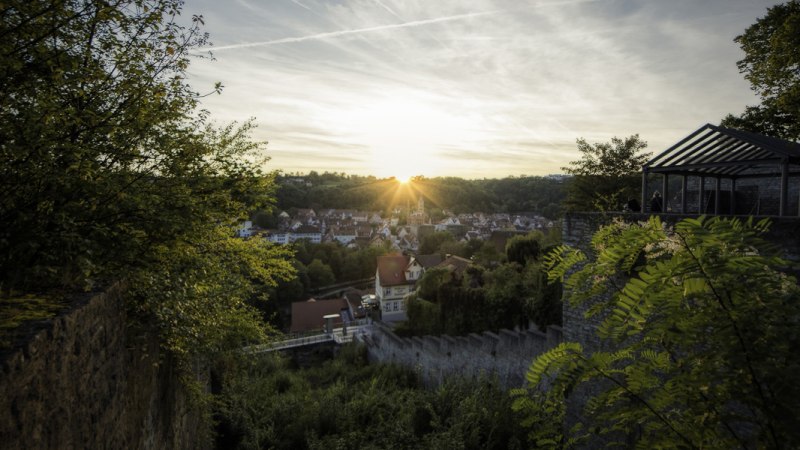 Sonnenuntergang über Schwäbisch Hall, gesehen von einer erhöhten Position mit Bäumen und alten Mauern im Vordergrund., © Patrick Krol