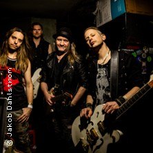 Vier Männer in Lederkleidung posieren mit Gitarren in einem dunklen Raum. Sie wirken lässig und rockig., © links im Bild