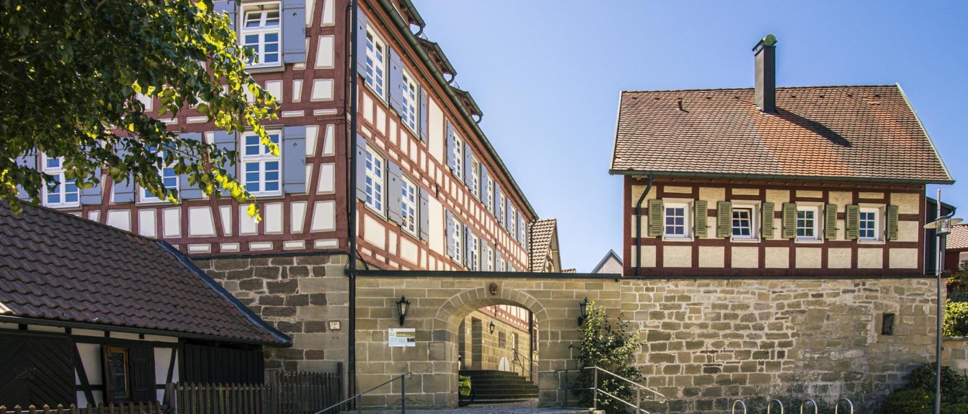 Fachwerkhäuser in der Altstadt von Murrhardt, Deutschland. Die Gebäude haben rote und weiße Fassaden mit blauen Fensterläden unter klarem Himmel., © SMG, Sarah Schmid Fachwerkhäuser in der Altstadt von Murrhardt, Deutschland. Die Gebäude haben rote und weiße Fassaden mit blauen Fensterläden unter klarem Himmel., © SMG, Sarah Schmid