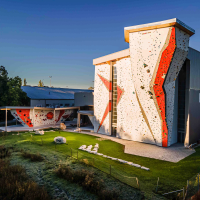 Kletterhalle mit hohen Kletterwänden und Boulderbereich im Freien, umgeben von Bäumen und Wiese, bei Sonnenuntergang., © Roccadion, Böblingen Kletterhalle mit hohen Kletterwänden und Boulderbereich im Freien, umgeben von Bäumen und Wiese, bei Sonnenuntergang., © Roccadion, Böblingen