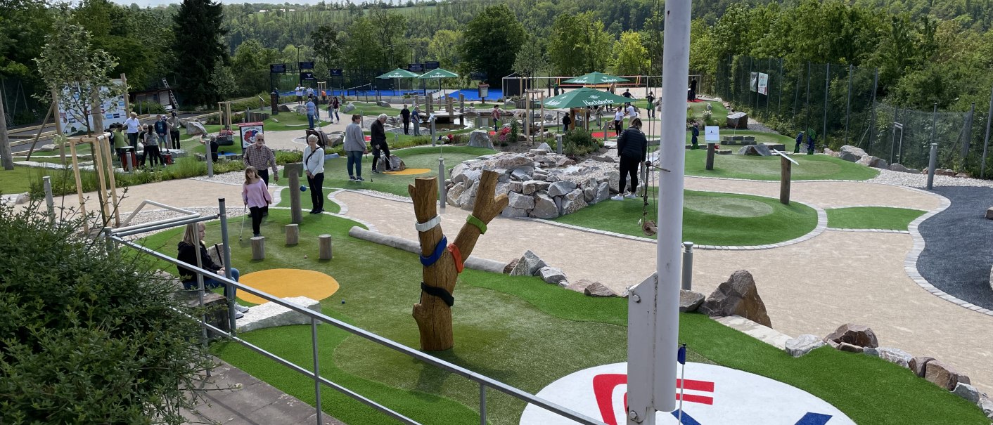 Abenteuer-Golfplatz in Vaihingen mit Spielern, Bäumen und Sonnenschirmen. Menschen genießen das Spiel bei sonnigem Wetter., © TC Vaihingen/Enz