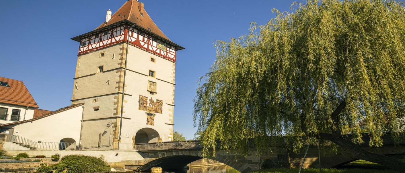 Das Beinsteiner Tor in Waiblingen mit Fachwerk und Brücke, umgeben von Bäumen, unter klarem Himmel., © SMG, Sarah Schmid Das Beinsteiner Tor in Waiblingen mit Fachwerk und Brücke, umgeben von Bäumen, unter klarem Himmel., © SMG, Sarah Schmid