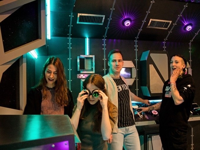Vier Personen in einem futuristischen Raum mit Lichtern und Konsolen. Eine Person trägt eine Brille, die anderen schauen interessiert umher., © ExitGames Stuttgart Vier Personen in einem futuristischen Raum mit Lichtern und Konsolen. Eine Person trägt eine Brille, die anderen schauen interessiert umher., © ExitGames Stuttgart