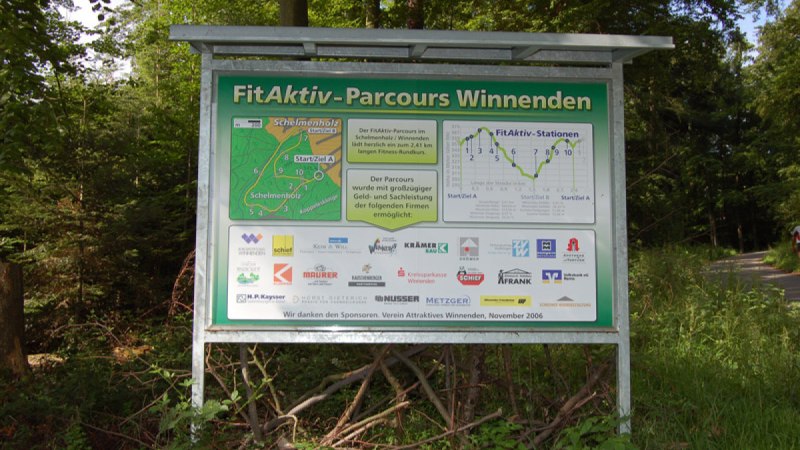 Schild des FitAktiv-Parcours Winnenden im Wald. Es zeigt eine Karte des Parcours und Logos von Sponsoren. Der Weg führt durch bewaldetes Gebiet., © Winnenden - Stuttgart-Marketing GmbH Schild des FitAktiv-Parcours Winnenden im Wald. Es zeigt eine Karte des Parcours und Logos von Sponsoren. Der Weg führt durch bewaldetes Gebiet., © Winnenden - Stuttgart-Marketing GmbH