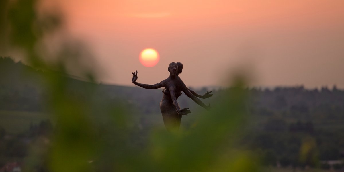 Eine Statue im Vordergrund vor einem orangefarbenen Sonnenuntergang, umgeben von unscharfem Gr&uuml;n., &copy; Stuttgart-Marketing GmbH