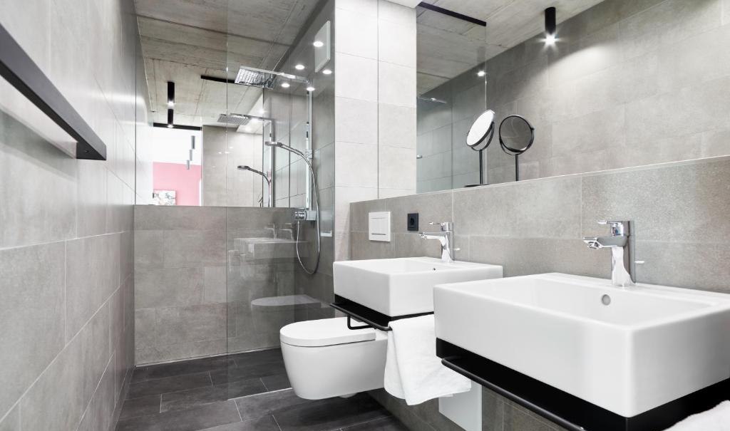 Modernes Badezimmer mit zwei Waschbecken, großer Spiegelwand, Regendusche und grauen Fliesen. Minimalistisches Design mit klaren Linien., © livisit bergapartments Modernes Badezimmer mit zwei Waschbecken, großer Spiegelwand, Regendusche und grauen Fliesen. Minimalistisches Design mit klaren Linien., © livisit bergapartments