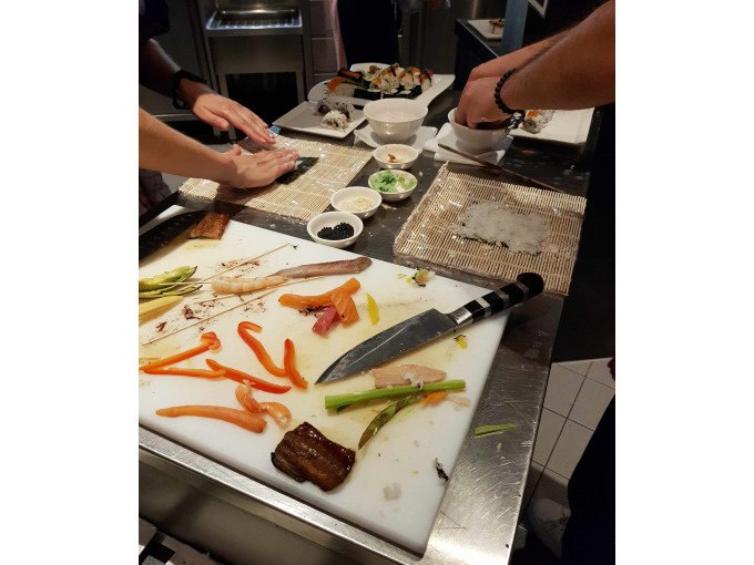 Zwei Personen bereiten Sushi auf einer Arbeitsfl&auml;che zu. Verschiedene Zutaten und ein Messer liegen auf einem Schneidebrett., &copy; Kultweine-Kochwelten-Kunst&uuml;cke - Kochschule Sonja Lenz