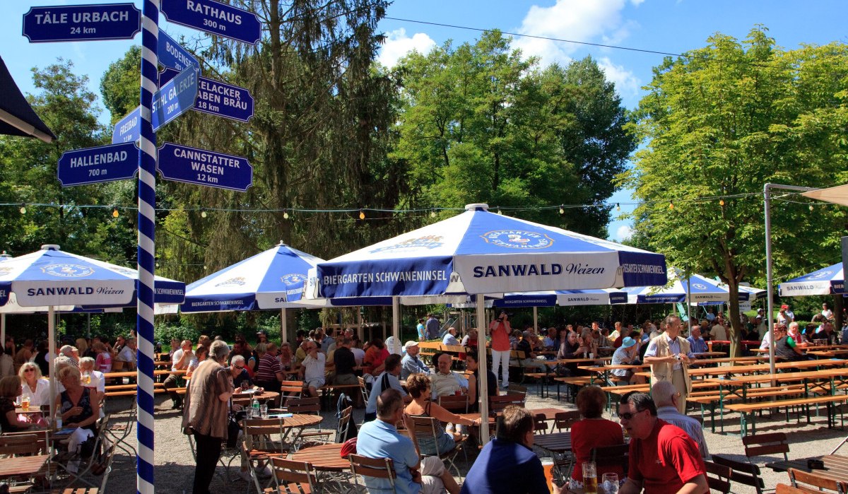 Ein belebter Biergarten mit Holztischen und -stühlen, blauen Sonnenschirmen und einem Wegweiser. Menschen genießen das sonnige Wetter., © Waiblingen - Stuttgart-Marketing GmbH Ein belebter Biergarten mit Holztischen und -stühlen, blauen Sonnenschirmen und einem Wegweiser. Menschen genießen das sonnige Wetter., © Waiblingen - Stuttgart-Marketing GmbH