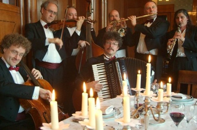 Musiker in Abendgarderobe spielen Instrumente um einen festlich gedeckten Tisch mit Kerzen., © Stadt Murrhardt