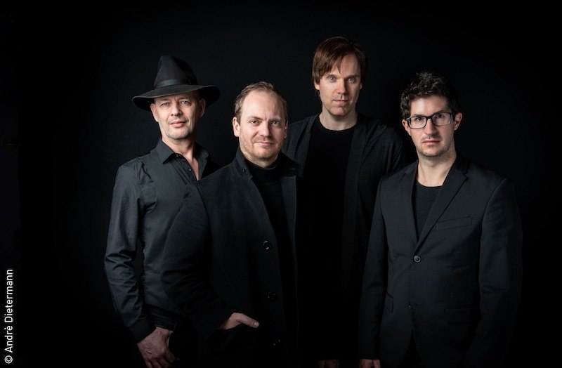 Vier Männer in schwarzer Kleidung posieren vor einem schwarzen Hintergrund. Einer trägt einen Hut, ein anderer eine Brille. Sie schauen ernst in die Kamera., © Stadt Kornwestheim Kulturmanagement