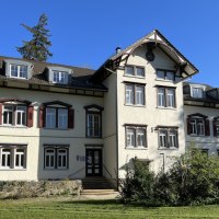 Ein historisches Geb&auml;ude mit wei&szlig;er Fassade und roten Fensterl&auml;den, umgeben von B&auml;umen und Rasen, bei strahlendem Sonnenschein., &copy; Stadt G&ouml;ppingen