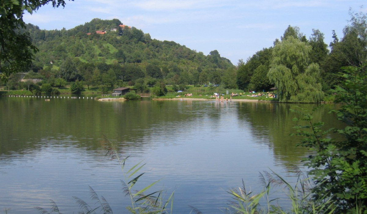 Ein See mit ruhigem Wasser, umgeben von grünen Hügeln und Bäumen. Menschen entspannen am Ufer., © Remstal Tourismus e.V. Ein See mit ruhigem Wasser, umgeben von grünen Hügeln und Bäumen. Menschen entspannen am Ufer., © Remstal Tourismus e.V.