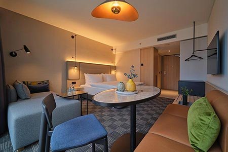 Modernes Hotelzimmer mit Doppelbett, Sofa, Tisch und Stühlen. Dezente Beleuchtung und stilvolle Dekoration schaffen eine gemütliche Atmosphäre., © Adina Apartment Hotel Stuttgart