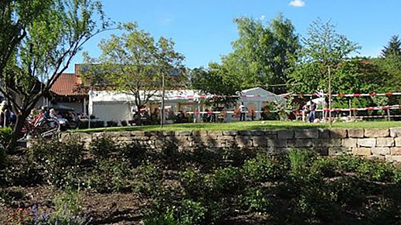 Ein Garten mit Bäumen und Menschen bei einem Fest. Im Hintergrund sind Zelte und ein Gebäude zu sehen. Der Himmel ist blau und sonnig., © Weingut Klopfer Ein Garten mit Bäumen und Menschen bei einem Fest. Im Hintergrund sind Zelte und ein Gebäude zu sehen. Der Himmel ist blau und sonnig., © Weingut Klopfer