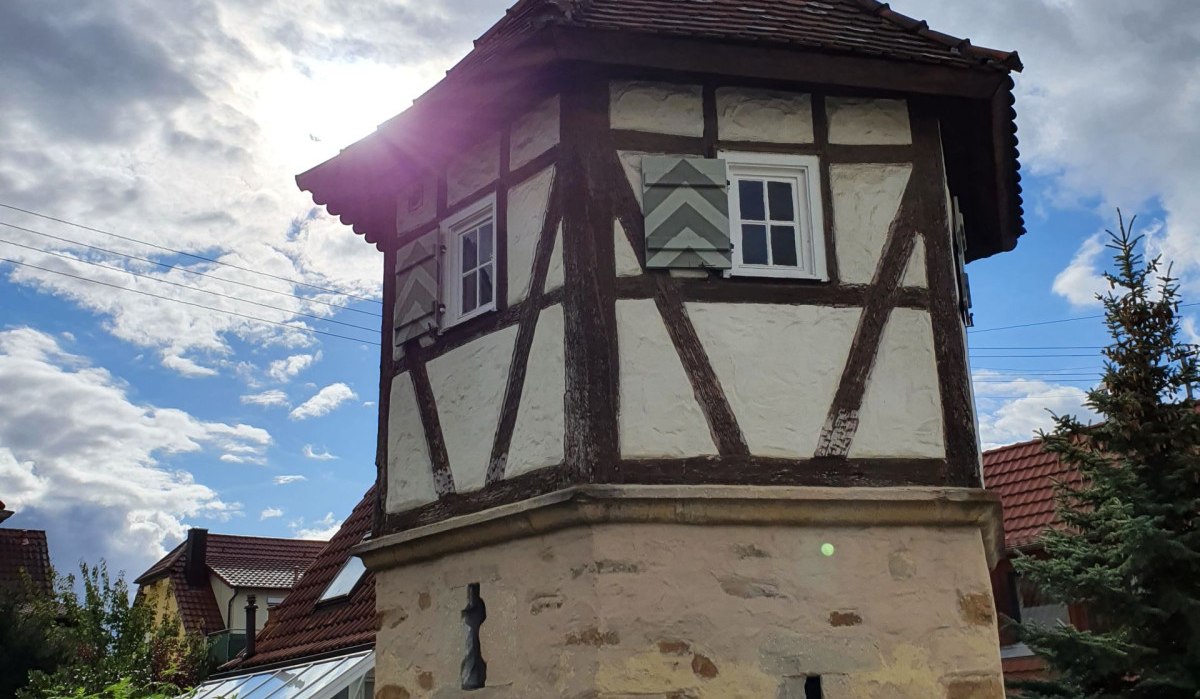 Ein Fachwerkturm mit Ziegeldach steht vor einem bewölkten Himmel. Die Sonne scheint hinter dem Turm hervor. Im Vordergrund ist eine Hecke zu sehen. Ein Fachwerkturm mit Ziegeldach steht vor einem bewölkten Himmel. Die Sonne scheint hinter dem Turm hervor. Im Vordergrund ist eine Hecke zu sehen.
