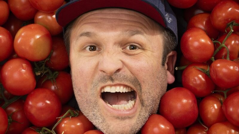 Ein Mann mit blauer Kappe schaut &uuml;berrascht aus einem Haufen Tomaten hervor. Sein Gesichtsausdruck ist lebhaft und humorvoll., &copy; Mauerwerk GmbH