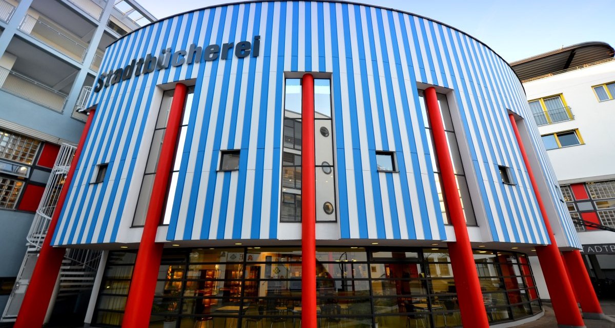 Die Stadtbücherei Fellbach zeigt eine Fassade mit blauen und weißen Streifen und roten Säulen. Moderne Architektur mit großen Fenstern., © Fellbach Tourismus Die Stadtbücherei Fellbach zeigt eine Fassade mit blauen und weißen Streifen und roten Säulen. Moderne Architektur mit großen Fenstern., © Fellbach Tourismus