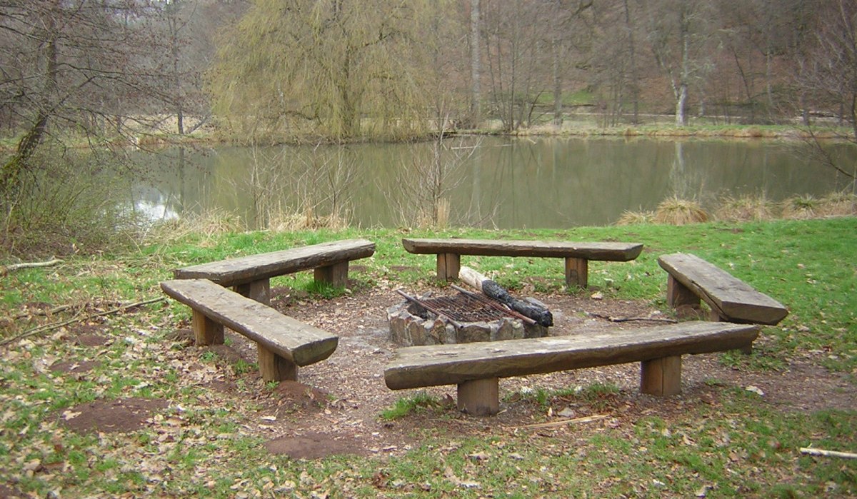 Holzbänke umgeben eine Feuerstelle in einem Waldgebiet, nahe einem ruhigen Teich. Die Umgebung ist herbstlich mit Laub auf dem Boden., © Naturpark Schönbuch Holzbänke umgeben eine Feuerstelle in einem Waldgebiet, nahe einem ruhigen Teich. Die Umgebung ist herbstlich mit Laub auf dem Boden., © Naturpark Schönbuch