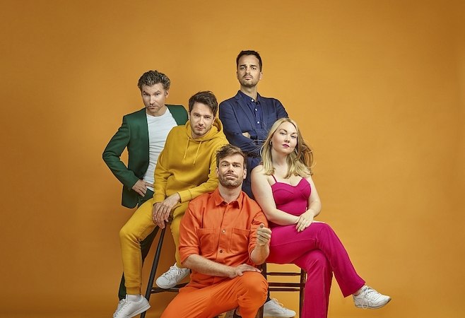 Fünf Personen in bunter Kleidung posieren vor einem orangefarbenen Hintergrund. Sie tragen Anzüge und Kleider in Grün, Gelb, Blau, Orange und Pink., © Stadthalle Leonberg