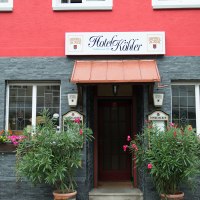 Das Hotel Köhler hat eine rote Fassade mit grauen Steinelementen. Vor dem Eingang stehen Pflanzen und bunte Blumen schmücken die Fenster., © Hotel Köhler Das Hotel Köhler hat eine rote Fassade mit grauen Steinelementen. Vor dem Eingang stehen Pflanzen und bunte Blumen schmücken die Fenster., © Hotel Köhler