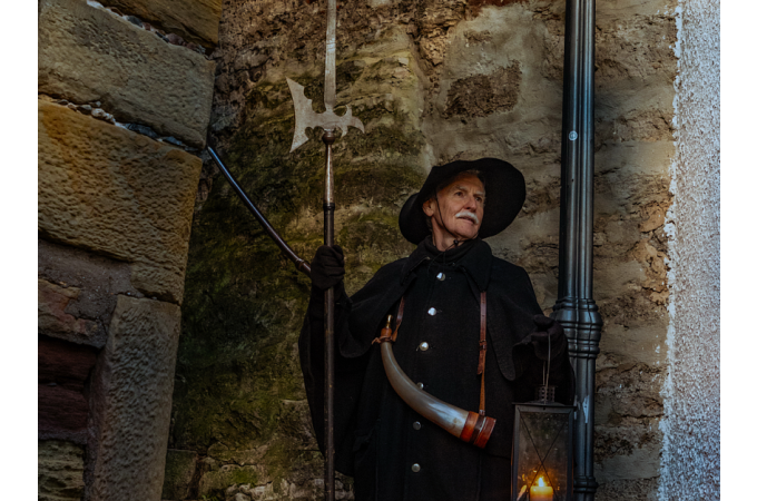Ein Nachtwächter in historischer Kleidung mit Laterne und Hellebarde steht vor einer alten Steinmauer., © Stadt Besigheim Ein Nachtwächter in historischer Kleidung mit Laterne und Hellebarde steht vor einer alten Steinmauer., © Stadt Besigheim