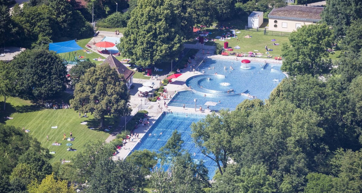 Luftaufnahme des Freibads in Kirchheim unter Teck mit Schwimmbecken, Liegewiese und Bäumen. Menschen entspannen und schwimmen bei sonnigem Wetter., © Schwäbische Alb Tourismusverband e.V. Luftaufnahme des Freibads in Kirchheim unter Teck mit Schwimmbecken, Liegewiese und Bäumen. Menschen entspannen und schwimmen bei sonnigem Wetter., © Schwäbische Alb Tourismusverband e.V.