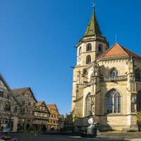 Die Schorndorfer Stadtkirche im Sonnenlicht, umgeben von Fachwerkhäusern und einem klaren blauen Himmel., © SMG, Sarah Schmid Die Schorndorfer Stadtkirche im Sonnenlicht, umgeben von Fachwerkhäusern und einem klaren blauen Himmel., © SMG, Sarah Schmid