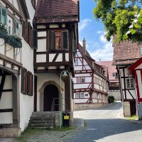 Fachwerkhäuser in der Sindelfinger Altstadt, mit blauen Fensterläden und Blumen. Kopfsteinpflasterstraße, Bäume und blauer Himmel im Hintergrund., © Wirtschaftsförderung Sindelfingen GmbH