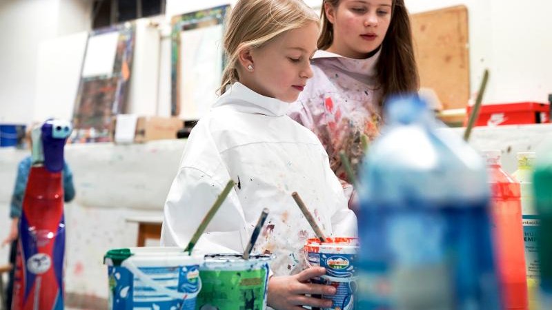 Zwei M&auml;dchen in einem Kunstworkshop, umgeben von bunten Farben und Pinseln. Sie tragen Malerkittel und sind konzentriert bei der Arbeit., &copy; Kunstschule Labyrinth