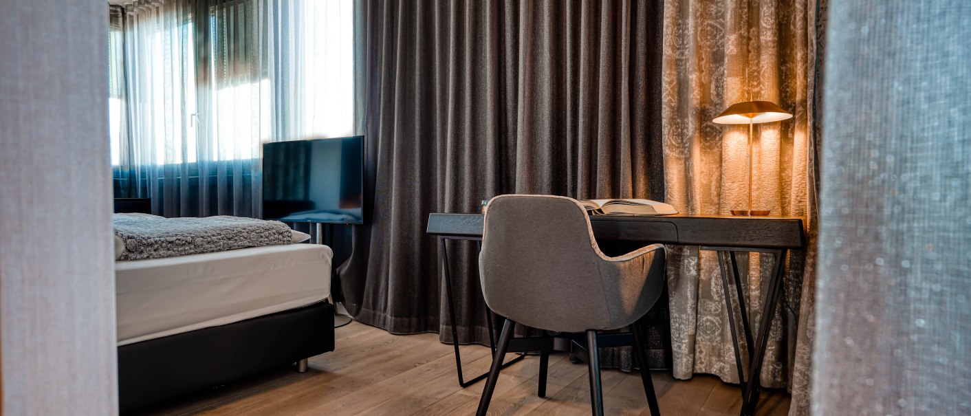 Moderne Penthouse-Suite mit Schreibtisch, Stuhl, Bett und Fernseher. Elegante Vorhänge und warme Beleuchtung schaffen eine gemütliche Atmosphäre., © CLOUD N°7 APARTMENTS GmbH