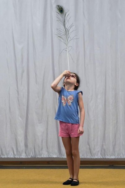 Ein Kind balanciert eine Pfauenfeder auf der Nase. Es trägt ein blaues Shirt mit Schmetterlingsmotiv und rosa Shorts., © Kunstschule Labyrinth Ein Kind balanciert eine Pfauenfeder auf der Nase. Es trägt ein blaues Shirt mit Schmetterlingsmotiv und rosa Shorts., © Kunstschule Labyrinth
