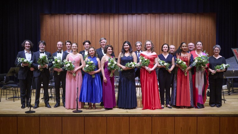 Eine Gruppe von Menschen in eleganter Abendkleidung steht auf einer B&uuml;hne und h&auml;lt Blumenstr&auml;u&szlig;e. Der Hintergrund ist eine Holzwand., &copy; www.peter-oppenlaender.de