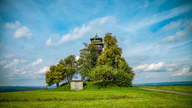 Der Hagbergturm in Gschwend steht auf einem H&uuml;gel, umgeben von B&auml;umen und einer gr&uuml;nen Wiese. Ein kleiner Weg f&uuml;hrt zum Turm, der Himmel ist blau mit Wolken., &copy; agentur arcos/Niki Eilers
