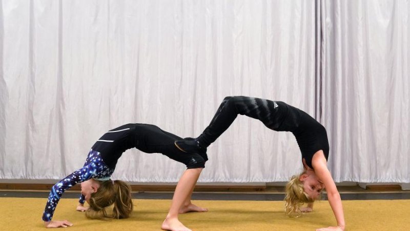 Zwei Kinder in Gymnastikanzügen formen eine Brücke auf einem Teppichboden vor einem weißen Vorhang., © Kunstschule Labyrinth
