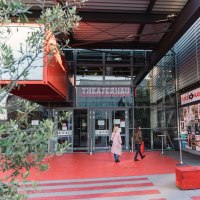 Eingang des Theaterhauses Stuttgart mit rotem Boden, Glasfassade und Plakaten. Zwei Personen betreten das Gebäude. Pflanzen und moderne Architektur sind sichtbar., © Stuttgart-Marketing GmbH, wpsteinheisser