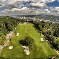 Luftaufnahme eines Golfplatzes in Stuttgart, umgeben von Bäumen und Hügeln, mit der Stadt im Hintergrund unter einem bewölkten Himmel., © GolfKultur Stuttgart Luftaufnahme eines Golfplatzes in Stuttgart, umgeben von Bäumen und Hügeln, mit der Stadt im Hintergrund unter einem bewölkten Himmel., © GolfKultur Stuttgart