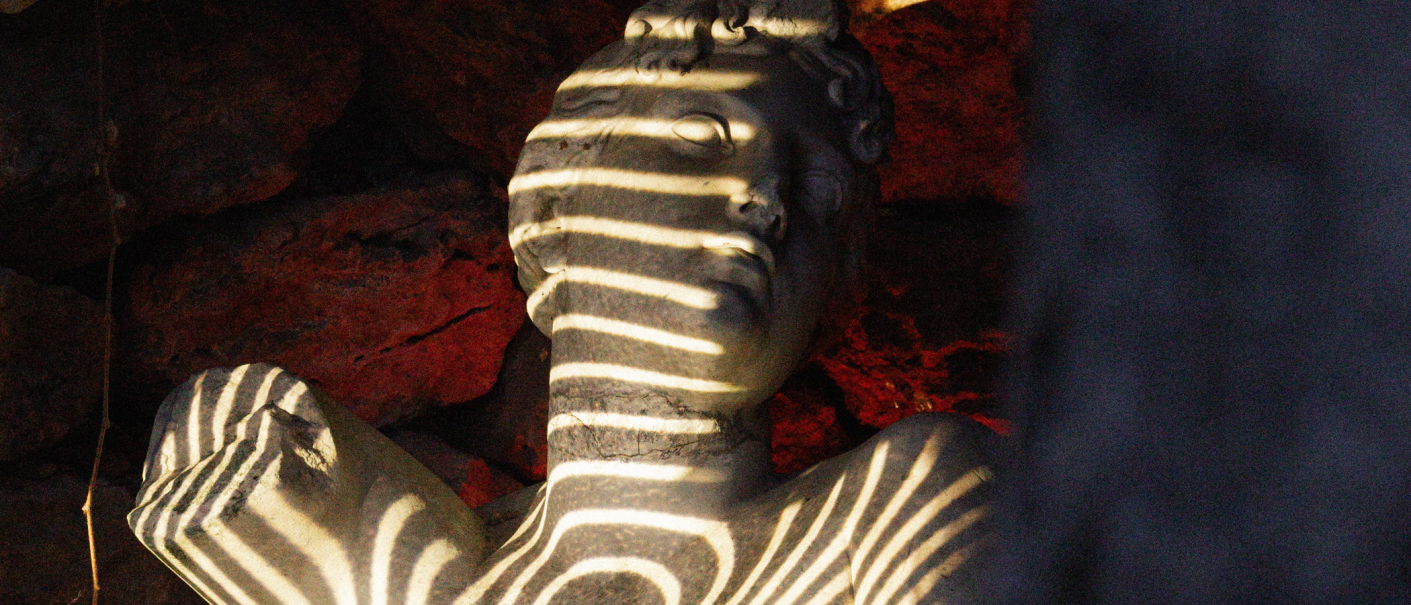 Eine Steinbüste mit Streifen aus Licht und Schatten, umgeben von einem rot-braunen Hintergrund., © Lichtgestalten Eine Steinbüste mit Streifen aus Licht und Schatten, umgeben von einem rot-braunen Hintergrund., © Lichtgestalten