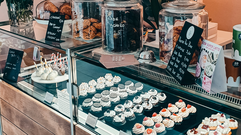 Eine Vitrine in einem Caf&eacute; zeigt eine Auswahl an Cupcakes, Cake Pops und Geb&auml;ck. Daneben stehen Gl&auml;ser mit Keksen und Preisschilder., &copy; Cupcakes & Bagels, Stuttgart