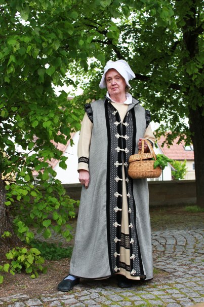 Eine Frau in historischer Kleidung h&auml;lt einen Korb und steht auf einem gepflasterten Weg unter einem Baum. Sie tr&auml;gt ein langes Gewand und eine wei&szlig;e Haube., &copy; Stadt Leonberg
