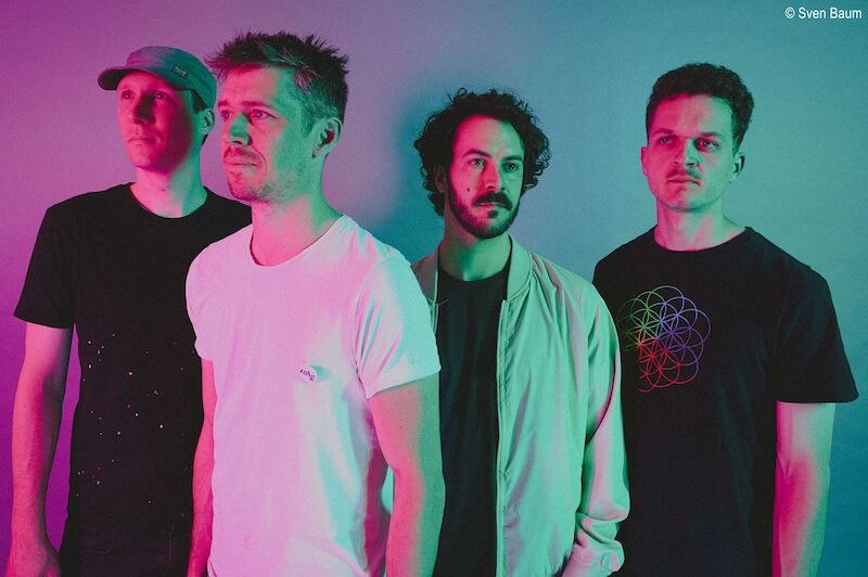 Vier M&auml;nner posieren vor einem farbigen Hintergrund, beleuchtet in pink und gr&uuml;n. Sie tragen l&auml;ssige Kleidung und blicken ernst in die Ferne., &copy; Stadthalle Leonberg