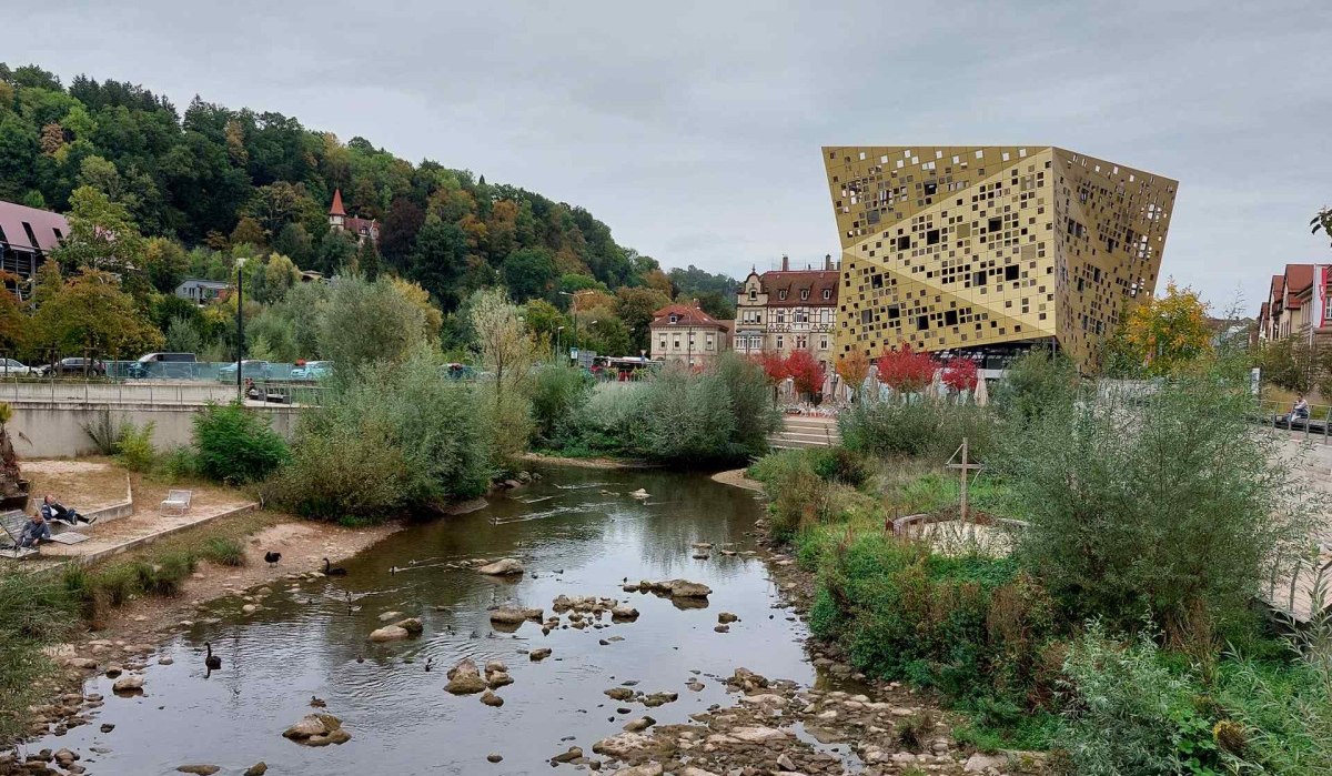 Goldenes Gebäude in Schwäbisch Gmünd neben einem Fluss, umgeben von Bäumen und alten Häusern., © Remstal Tourismus e.V. I Architekt: isin Architekten