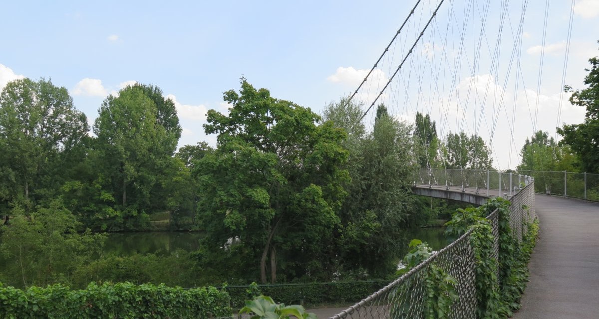 Der Max-Eyth-Steg ist eine Fußgängerbrücke, die über einen Fluss führt, umgeben von üppigem Grün und Bäumen. Der Himmel ist leicht bewölkt., © Stuttgart-Marketing GmbH Der Max-Eyth-Steg ist eine Fußgängerbrücke, die über einen Fluss führt, umgeben von üppigem Grün und Bäumen. Der Himmel ist leicht bewölkt., © Stuttgart-Marketing GmbH