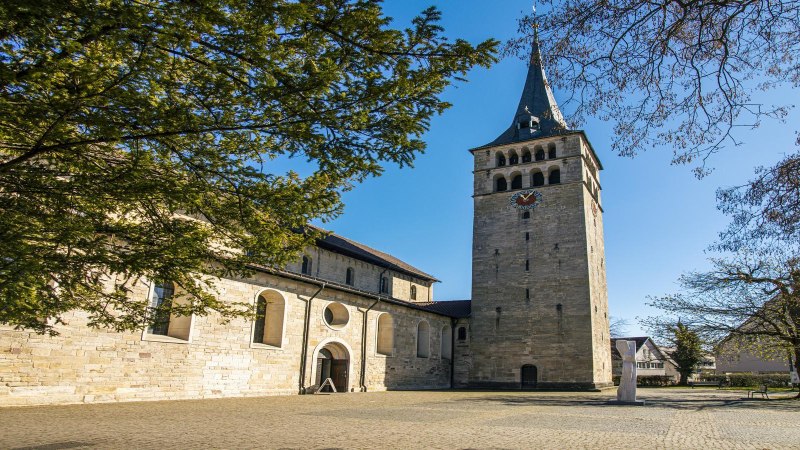 Die Martinskirche Sindelfingen mit ihrem markanten Turm, umgeben von Bäumen und einem gepflasterten Platz, unter klarem blauem Himmel., © SMG, Sarah Schmid