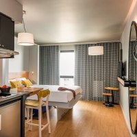 Modernes Studio mit Küchenzeile, Esstisch und Bett. Große Spiegel und Fenster, helle Einrichtung mit Holzboden und stilvollen Möbeln., © adagio access Stuttgart Airport Messe